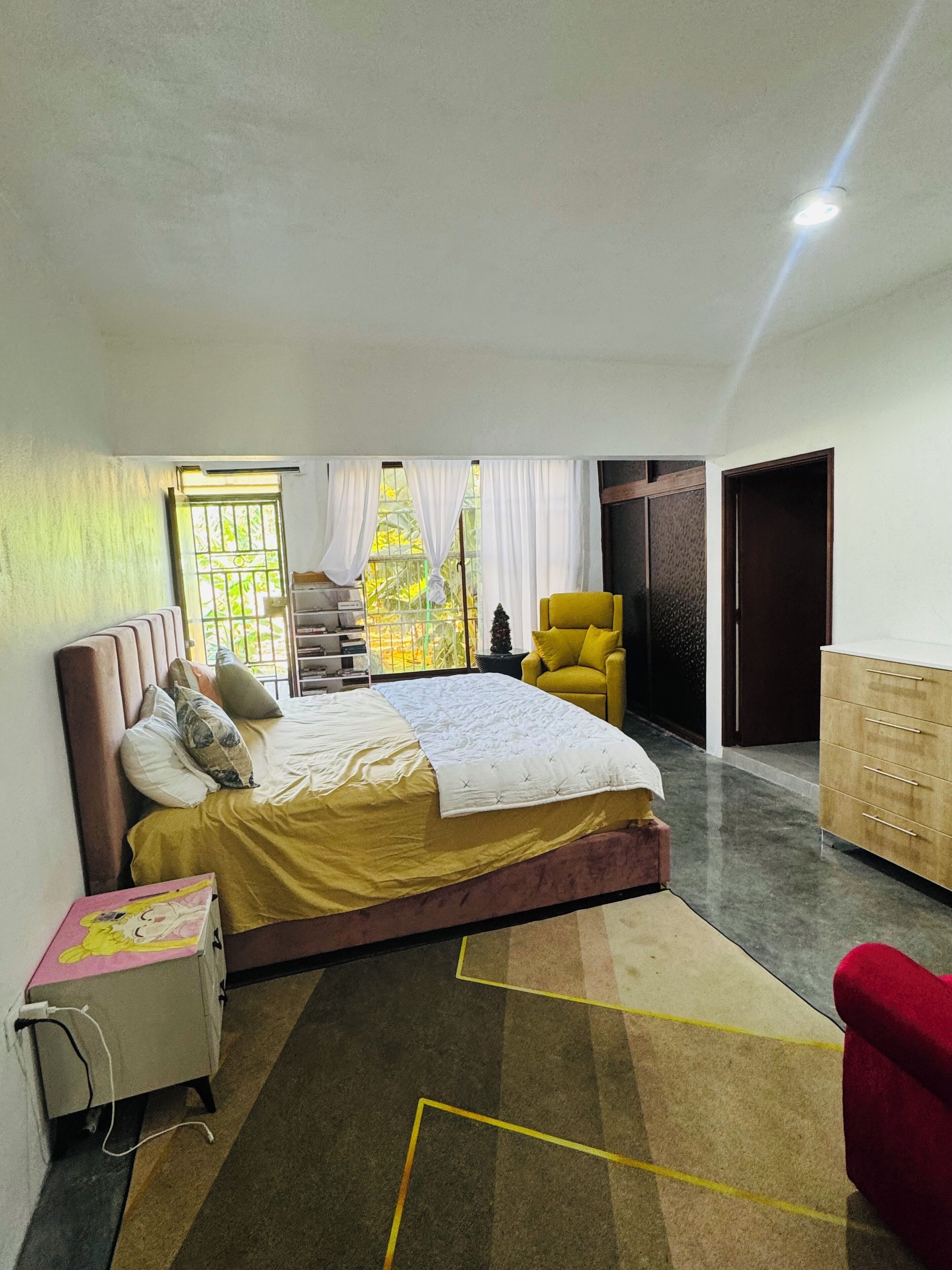 Une chambre à coucher avec un lit, une chaise, une commode et une fenêtre avec des rideaux.