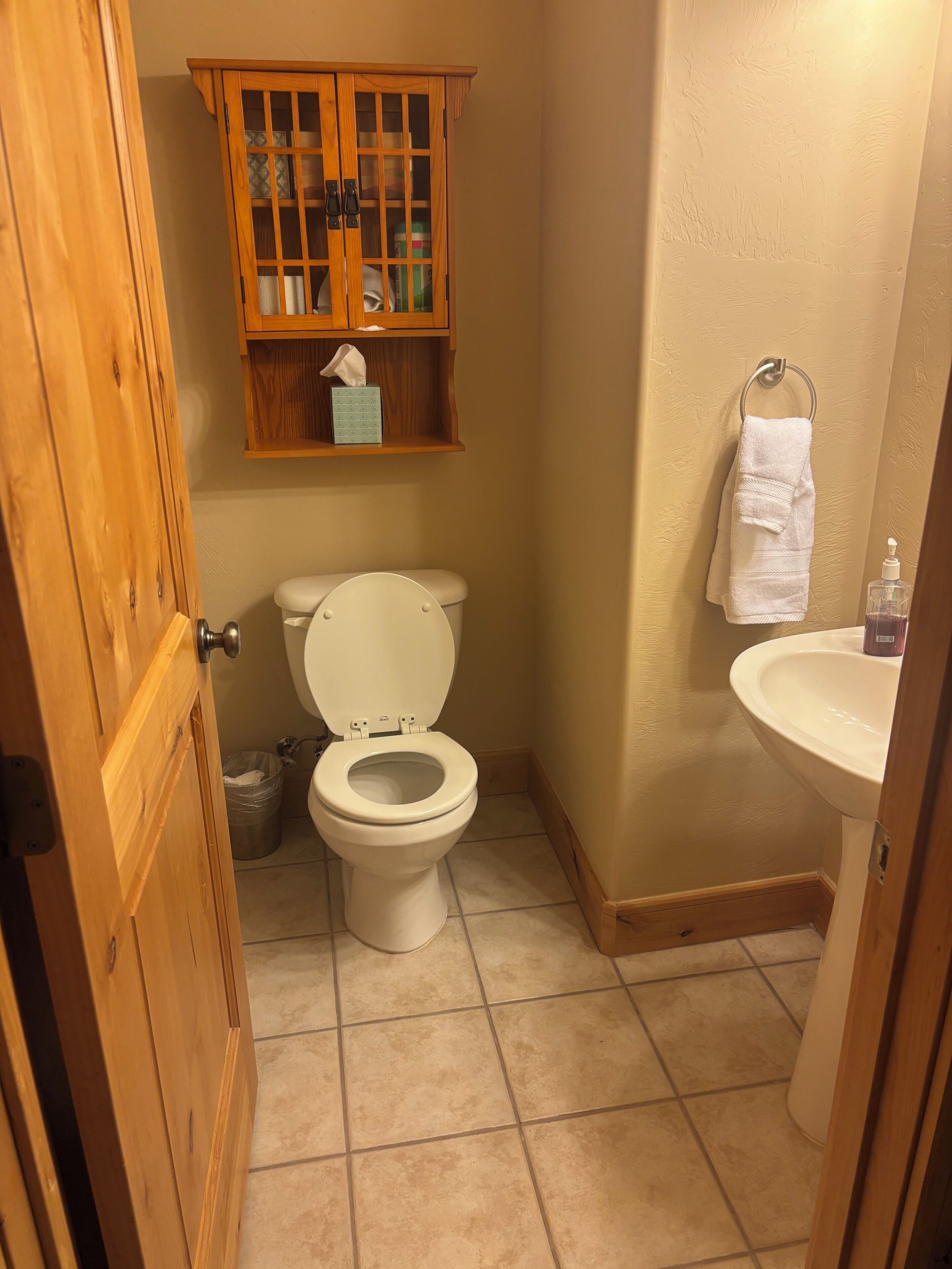 Un baño con inodoro, un armario de madera encima y un lavabo con una toalla colgada en la pared.