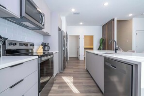 A modern kitchen with stainless steel appliances, a dishwasher, and a countertop with a sink. - Designer Disney Escape with Themed Rooms (Kissimmee)