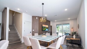 Un espace repas moderne avec une table à plateau en verre, des chaises blanches et un luminaire suspendu.