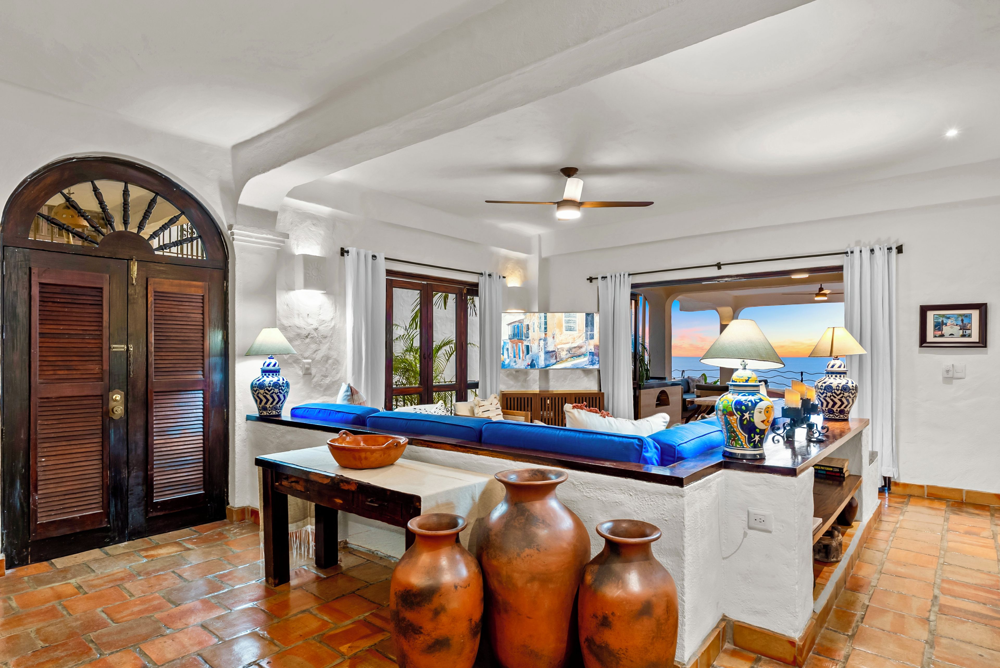 A spacious living area with a large window, a blue sofa, a wooden table, and a decorative vase.
