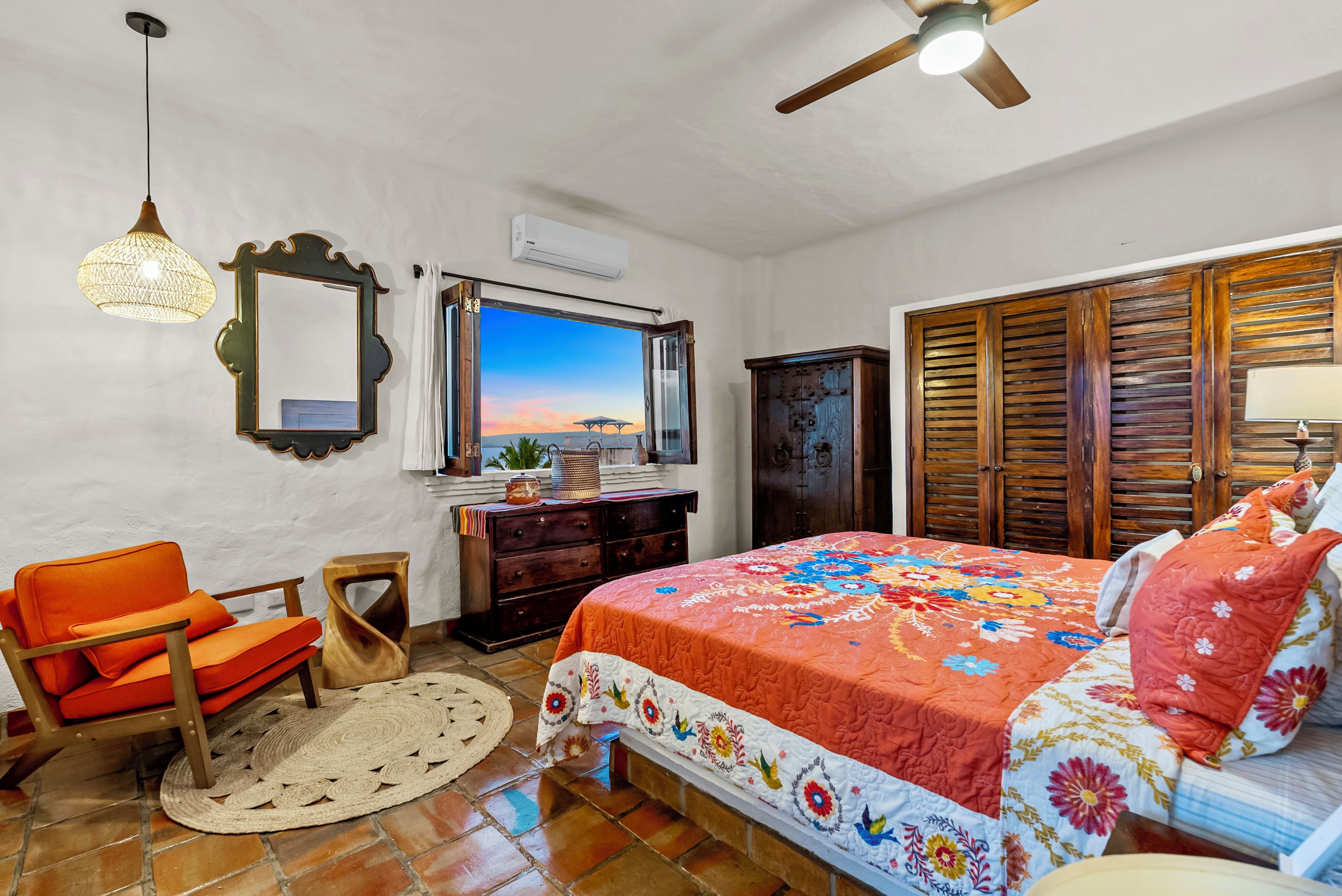 Ein Schlafzimmer mit einem Bett, einem Sessel, einer Kommode, einem Spiegel und einem Deckenventilator.