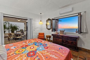 Une chambre d’hôtel comprenant un lit, une commode, une chaise, un coin repas et une vue sur la mer.