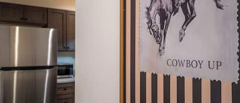 A kitchen with stainless steel appliances and a framed artwork depicting a horse with the text 'COWBOY UP'.