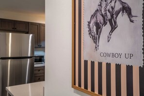 A kitchen with stainless steel appliances and a framed artwork depicting a horse with the text 'COWBOY UP'. - Iron Horse at Hoff & Co | Off 4th Ave (Tucson)