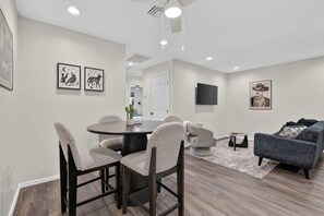 A modern living room with a dining area, a flat-screen TV mounted on the wall, and artwork on the walls. - Iron Horse at Hoff & Co | Off 4th Ave (Tucson)