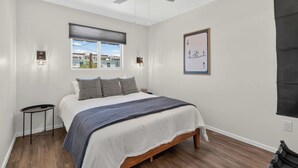 A bedroom with a bed, a ceiling fan, a window with blinds, a wall-mounted light, and a framed picture. - Iron Horse at Hoff & Co | Off 4th Ave (Tucson)
