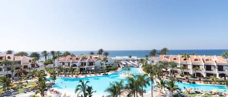 A resort with a large pool, multiple lounge areas, and a view of the ocean.