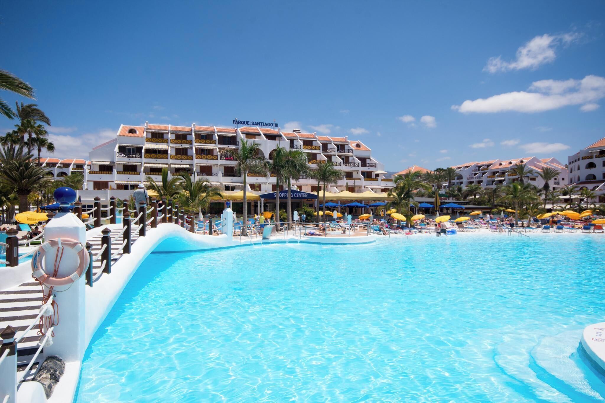 Et hotel med en stor swimmingpool, flere altaner og et skilt til shoppingcenteret.