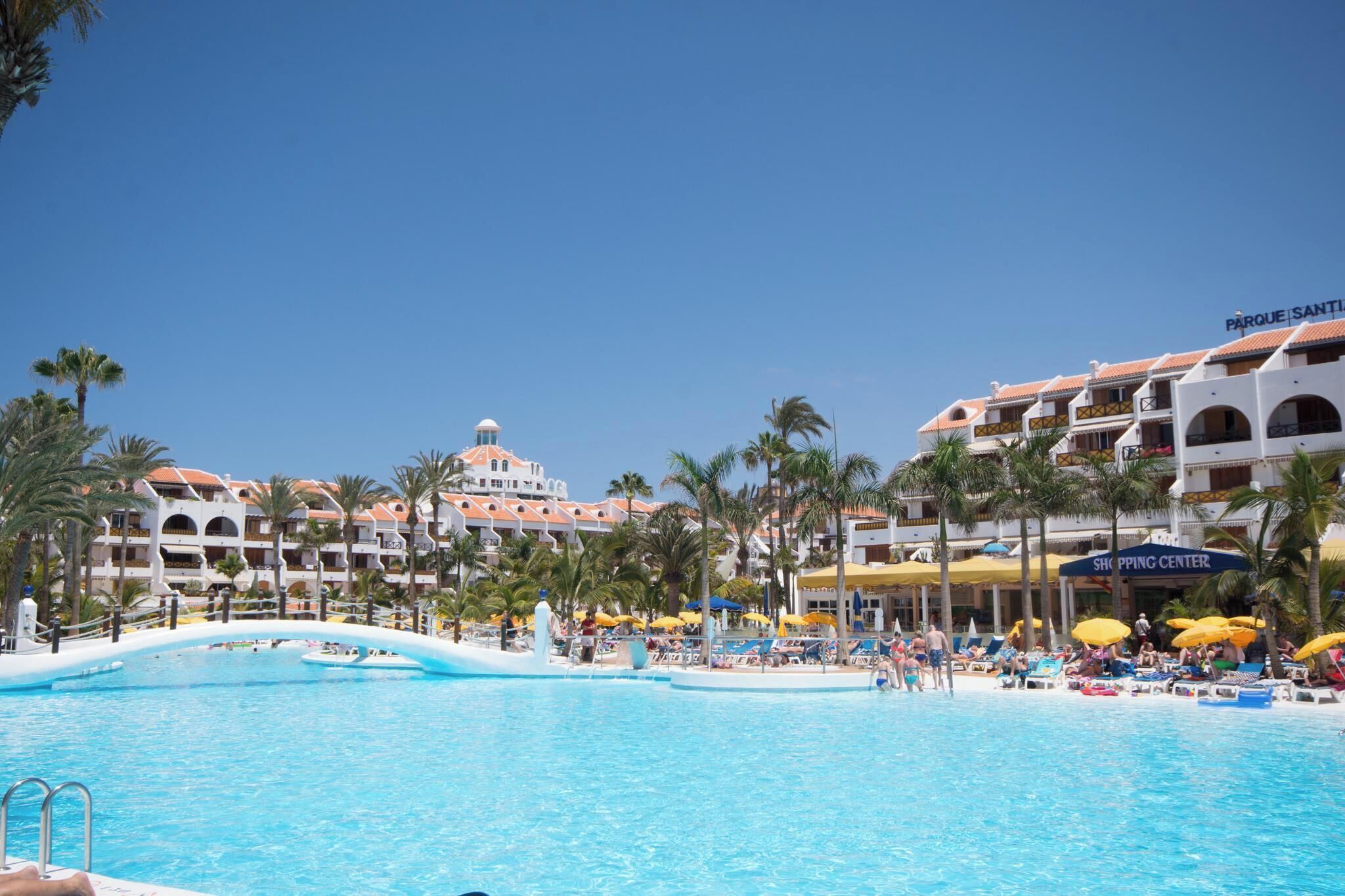 A resort with a swimming pool, palm trees, and a shopping center.