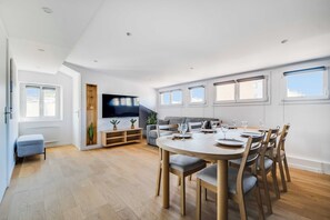 A modern living room with a dining area, wooden flooring, a flat-screen TV, and large windows. - Spacious Apartment 2ch/6p - Boulogne-billancourt (Boulogne-Billancourt)