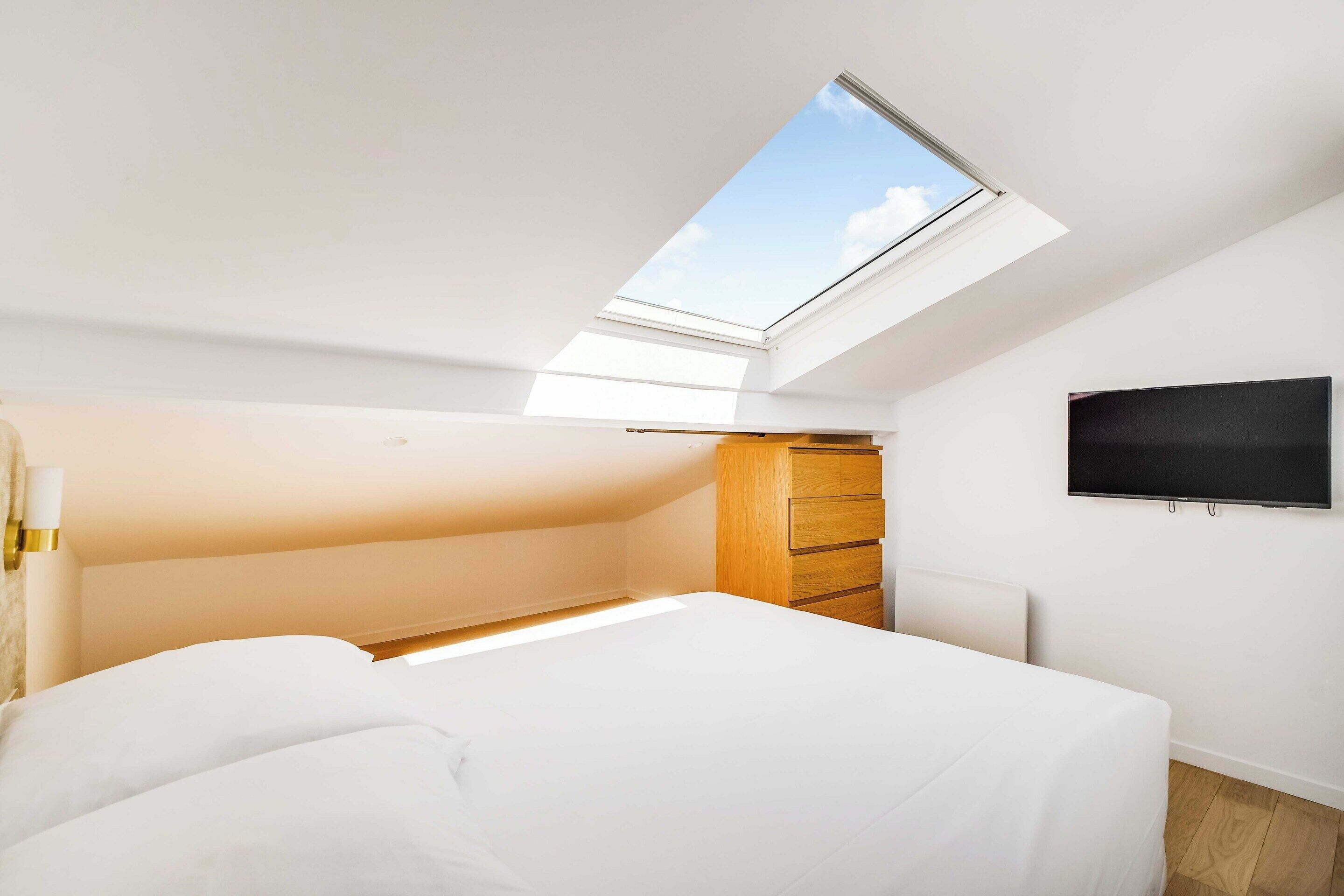 A bedroom with a skylight, a bed, a wardrobe, and a flat-screen TV.