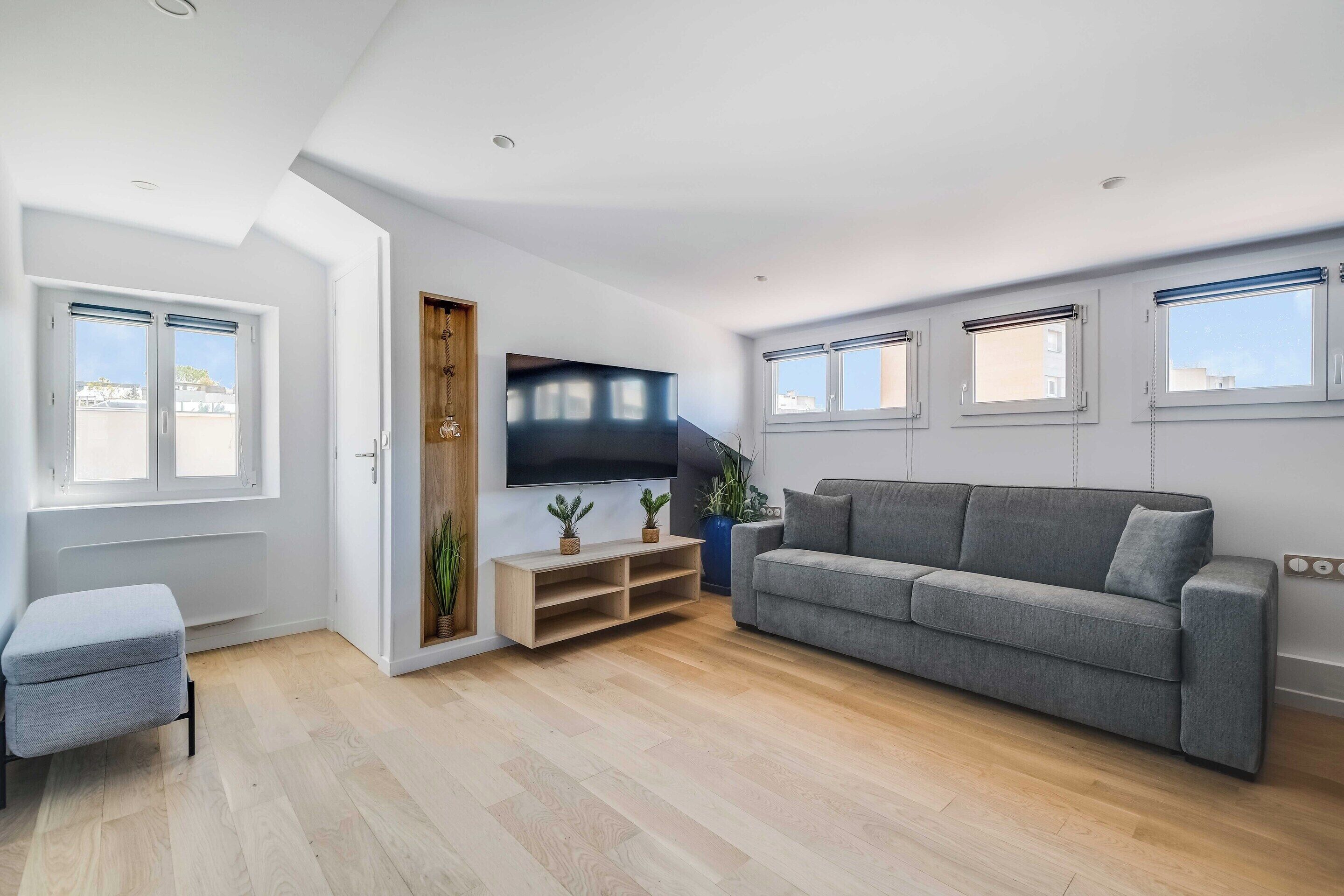 A modern living room with a grey sofa, a TV, and a wooden entertainment unit.