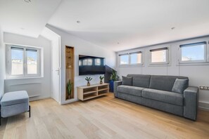 A modern living room with a grey sofa, a TV, and a wooden entertainment unit. - Spacious Apartment 2ch/6p - Boulogne-billancourt (Boulogne-Billancourt)