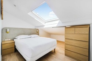 Un dormitorio con tragaluz, una cama, mesitas de noche de madera y un armario.