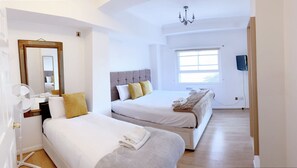 A hotel room with two beds, a large mirror, a fan, and a television.