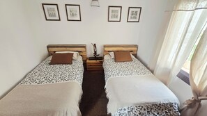 A room with two beds, a wooden headboard, a nightstand, and a wall-mounted lamp. - The Haven of Happiness (Fataga)