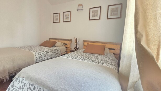 Ein Zimmer mit zwei Betten, jedes mit einer gemusterten Tagesdecke und einem Holzkopfstück. An der Wand ist eine Leuchte angebracht und über den Betten befindet sich gerahmte Kunst.