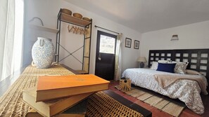 A bedroom with a bed, a nightstand, a lamp, a door, and a window. - The Haven of Happiness (Fataga)