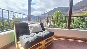 Ein Balkon mit einer Holzpaletten-Couch, einem kleinen Tisch mit einer Pflanze und Blick auf Berge und Grün.