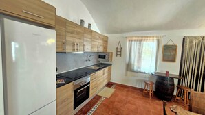 Eine kompakte Küche mit Kühlschrank, Mikrowelle und Backofen. Ein Fenster mit Vorhängen und ein kleiner Hocker sind ebenfalls vorhanden.