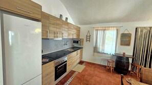 Eine kompakte Küche mit Kühlschrank, Mikrowelle und Backofen. Ein Fenster mit Vorhängen und ein kleiner Hocker sind ebenfalls vorhanden.