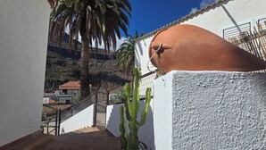 Ein Balkon mit Blick auf eine gebirgige Landschaft, ein Kaktus und eine weiße Wand mit einem Terrakotta-Topf.
