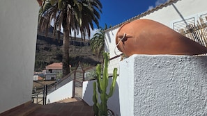 Ein Balkon mit Blick auf eine gebirgige Landschaft, ein Kaktus und eine weiße Wand mit einem Terrakotta-Topf.
