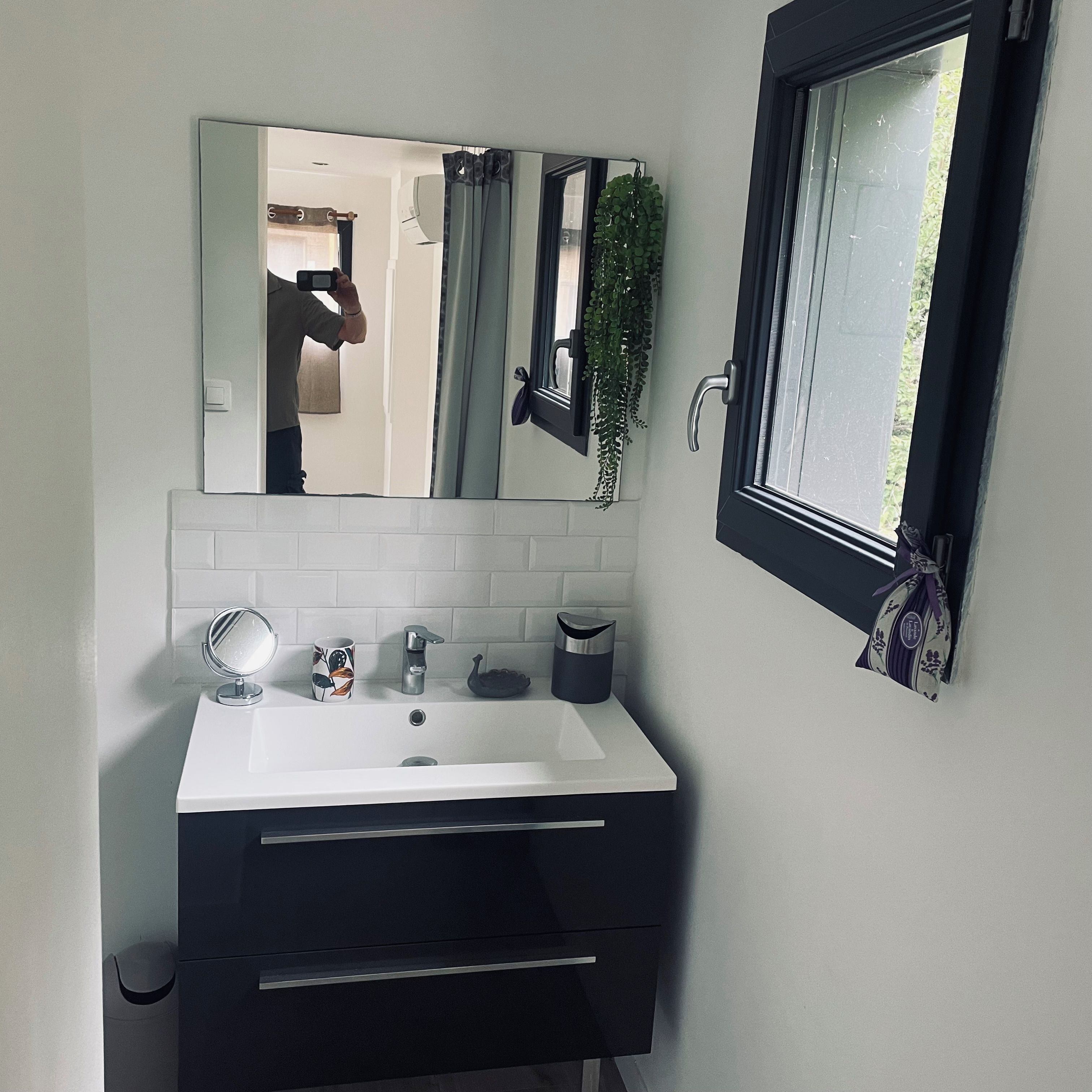 Un baño con un lavamanos blanco, un espejo, un perchero para toallas y una ventana con vistas al verdor.