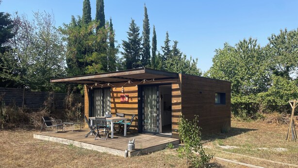 A small wooden cabin with a patio, a table, and chairs.