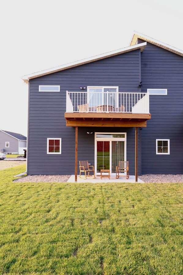 A two-story building with a balcony, a covered entryway, and a grassy yard.