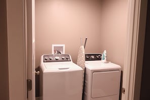 A laundry room with a front-loading washer and dryer, a towel rack, and a small shelf with a bottle.