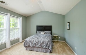 A bedroom with a bed, a window with blinds, a bedside table, and a wall-mounted picture.