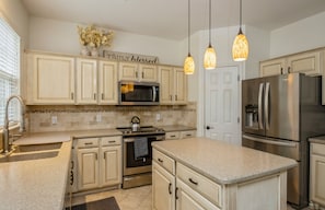 A modern kitchen with white cabinetry, stainless steel appliances, and pendant lighting.