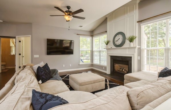 A living room with a sectional sofa, a flat-screen TV, a fireplace, and a ceiling fan.