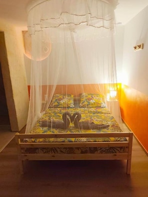 A bed with a canopy, a bedside lamp, and a patterned bedspread. - Flaming Ti (Deshaies)
