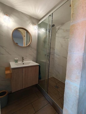 A bathroom with a glass shower enclosure, a round mirror, and a wooden vanity with a sink. - Flaming Ti (Deshaies)