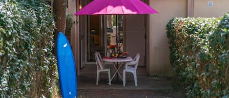Un espace extérieur aménagé avec une table et des chaises, une planche de surf et un grand parasol.