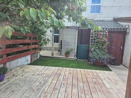 A wooden deck with a small lawn area, a red fence, and a building with a window and a door.
