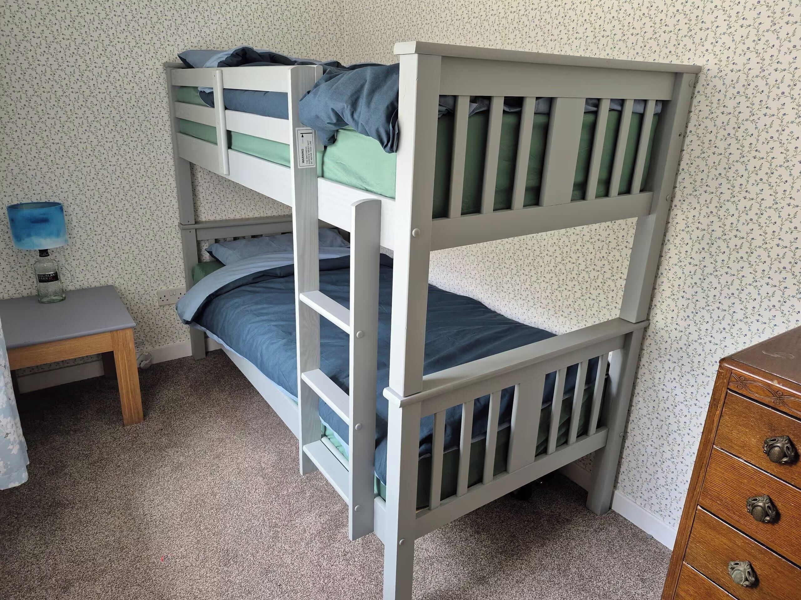A bunk bed with a desk and dresser in a room with floral wallpaper.