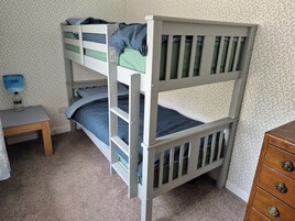 A bunk bed with a desk and dresser in a room with floral wallpaper.