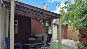 Un patio techado con mesa y sillas, cerca de madera y césped verde.