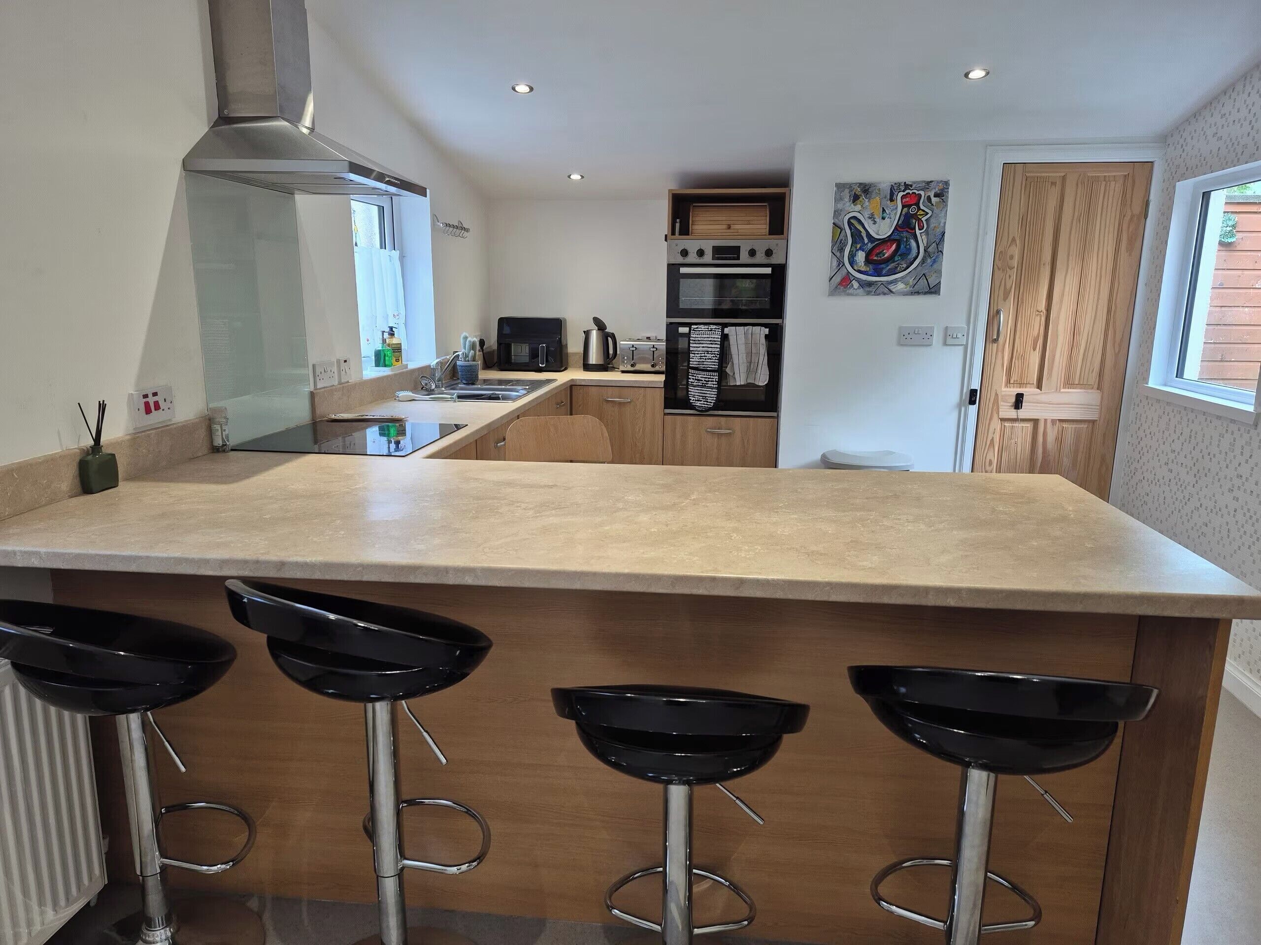 A modern kitchen with a central island, bar stools, a microwave, and a wooden door.