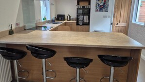 Una cocina moderna con una isla central, taburetes de bar, microondas y una puerta de madera.