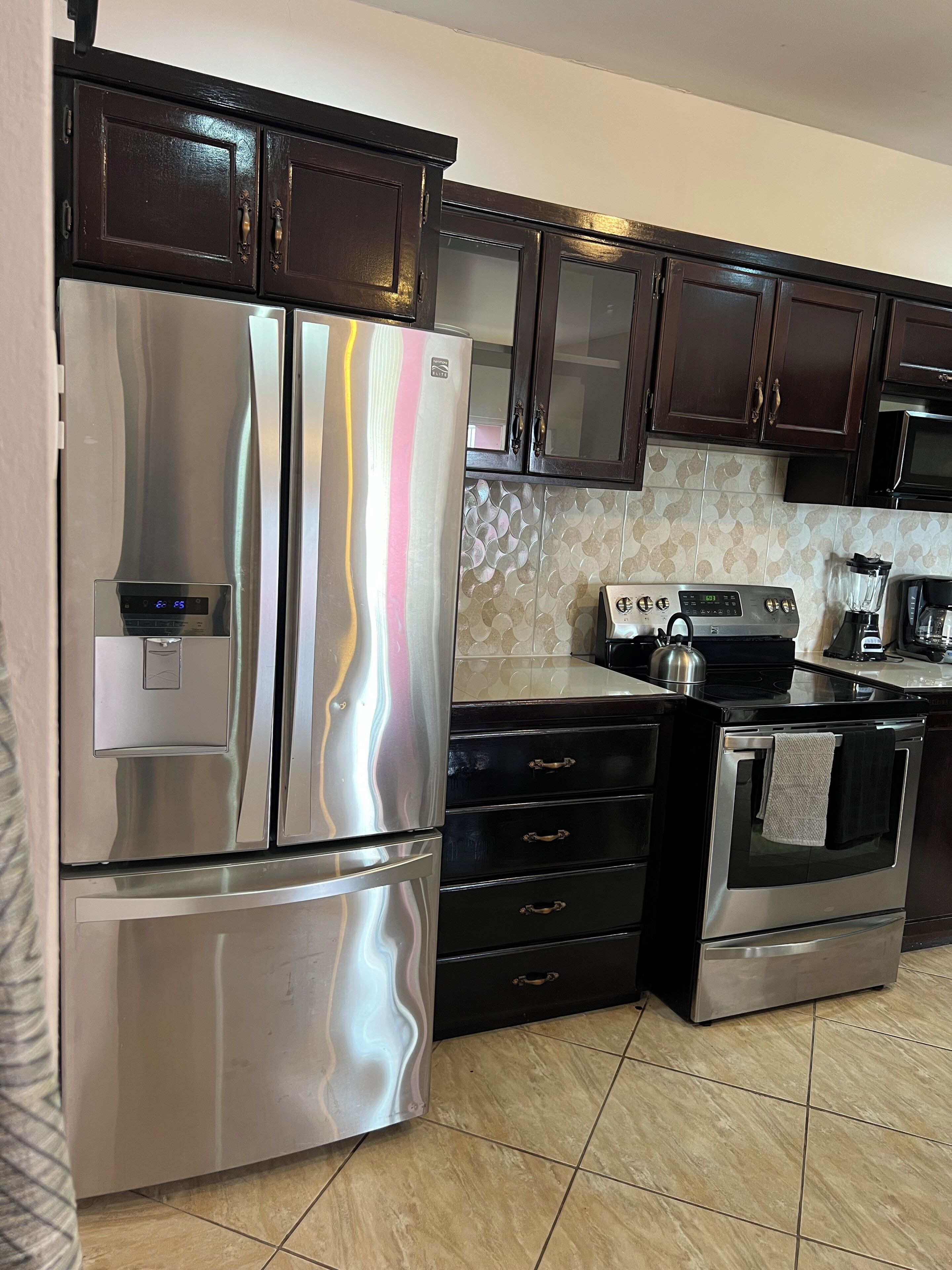 A kitchen with stainless steel appliances, dark wooden cabinets, and a patterned backsplash.