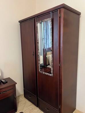 Une armoire avec un miroir, une table de chevet et un lit avec une tête de lit.