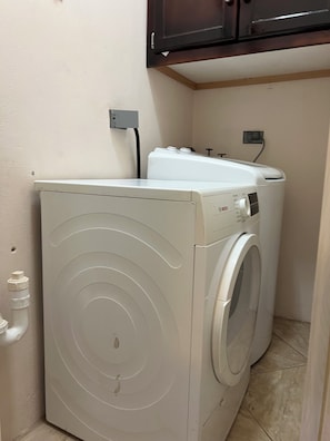 Ein kleiner Hauswirtschaftsraum mit einer Waschmaschine und einem Trockner mit Frontlader, einer fest installierten Steckdose und einem Holzschrank darüber.