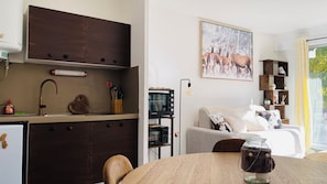 A compact kitchen with dark cabinets, a built-in oven, and a dining area with a table. - Cozy Studio (Formiguères)