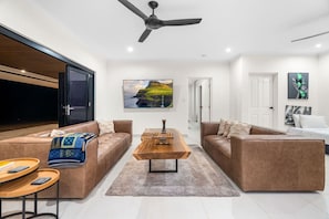 A modern living room with leather sofas, a wooden coffee table, and a ceiling fan.