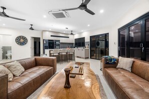 A modern living room with leather sofas, a wooden coffee table, and a kitchen in the background.